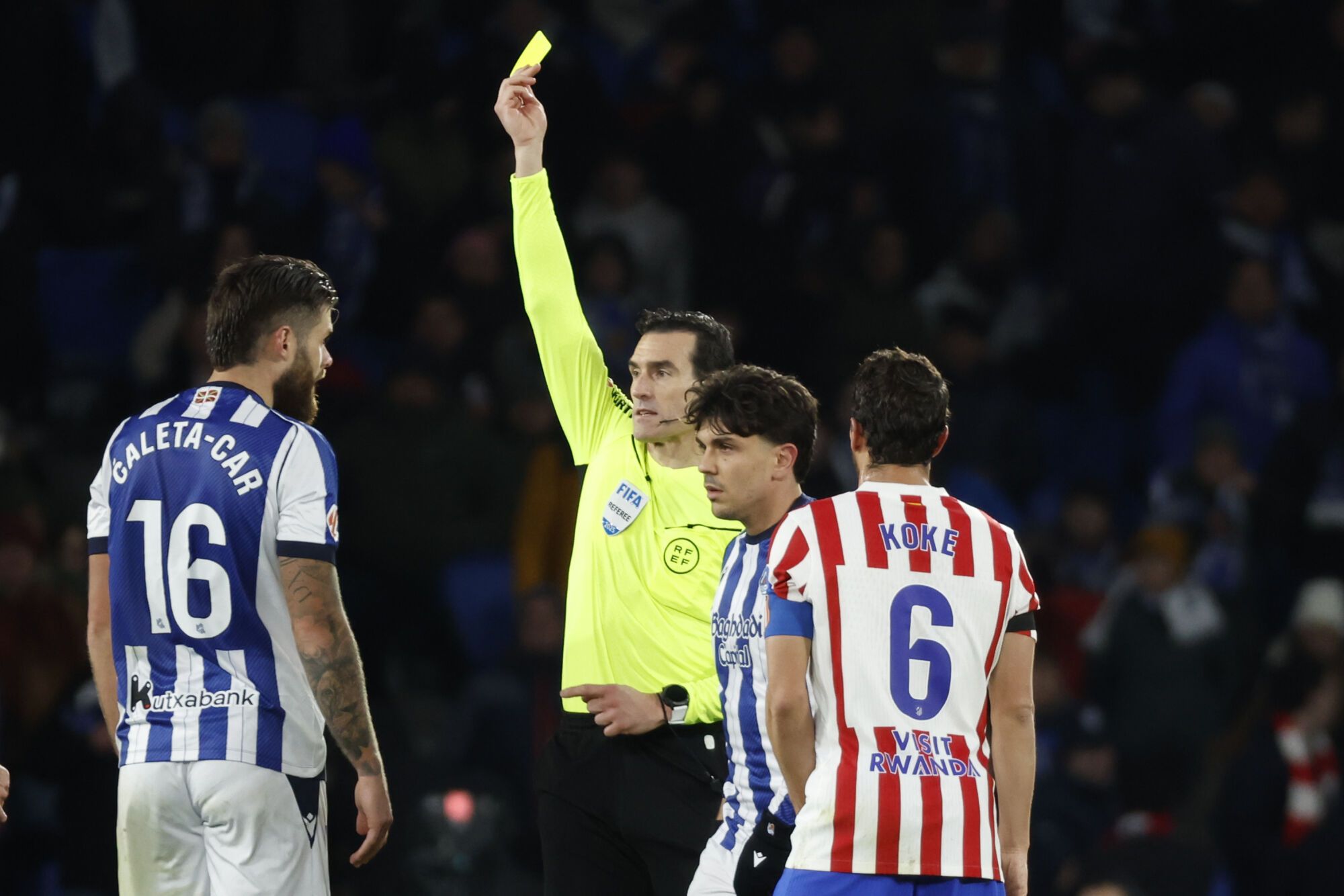 GRAF3374. SAN SEBASTIÁN, 04/01/2026.- El árbitro del partido Martínez Munuera saca tarjeta amarilla a Duje Caleta-Car (i), de la Real Sociedad, durante el partido de la jornada 18 de LaLiga que Real Sociedad y Atlético de Madrid disputan hoy domingo en el estadio de Anoeta. EFE/Juan Herrero