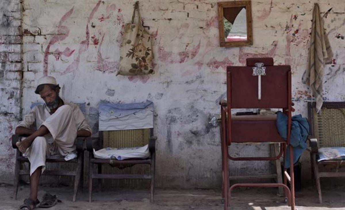 Un barber de carrer pakistanès fa un descans a l’espera de clients, en una carretera de Rawalpindi (Pakistan).