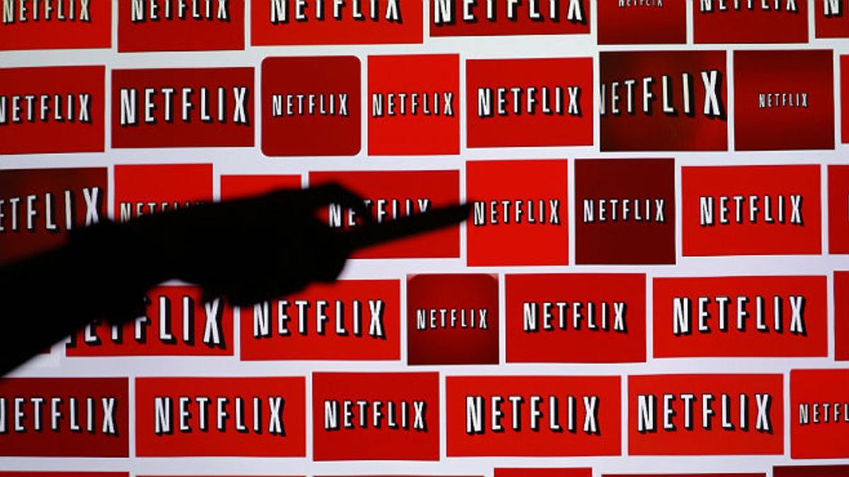 Sombra de un hombre sujetando un mando a distancia sobre el fondo del logo de Netflix.