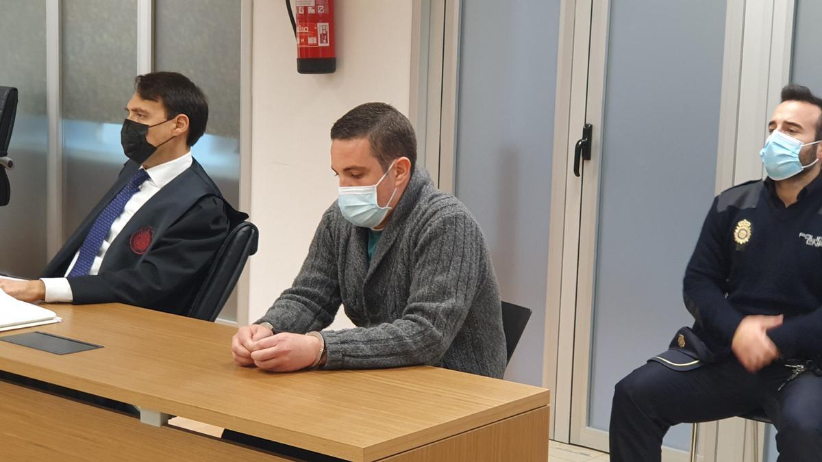 El acusado de matar a su madre y acuchillar al padre, entre su abogado José Manuel Ortigosa Lora y un policía nacional en el juicio celebrado en Alicante.