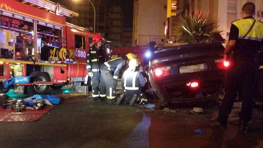 Los bomberos atienden al conductor del vehículo, volcado en la calzada.