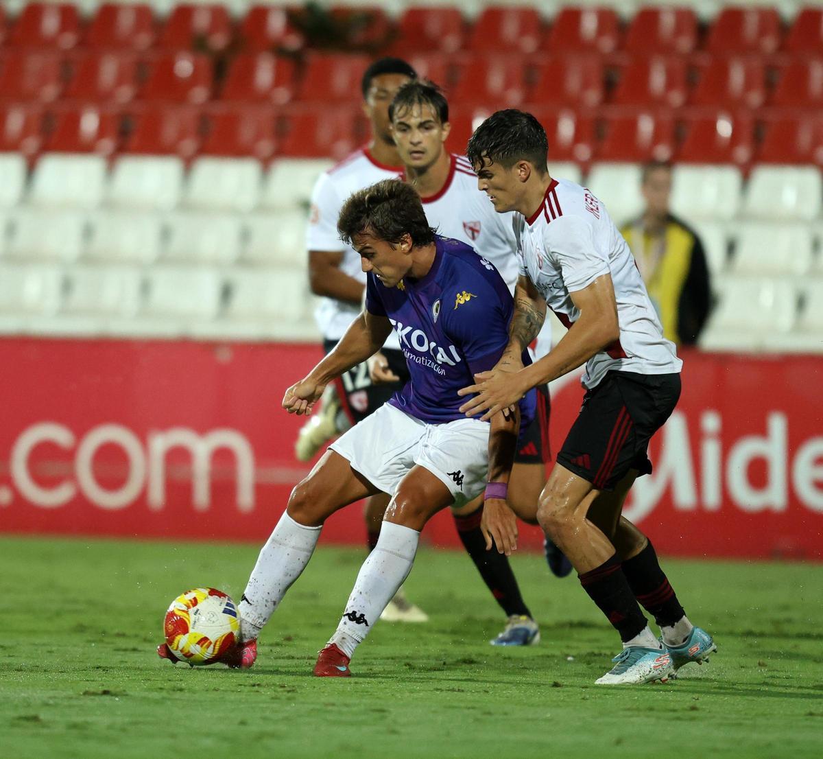 Slavy protege el balón presionado por dos defensores del Sevilla Atlético.