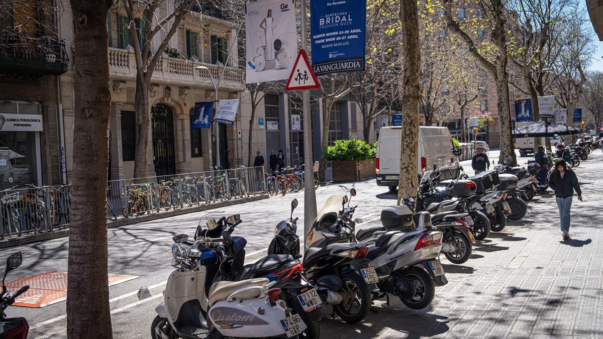 Motos estacionadas en la acera, bajo el cartel de zona escolar, frente a la Escola Diputació.