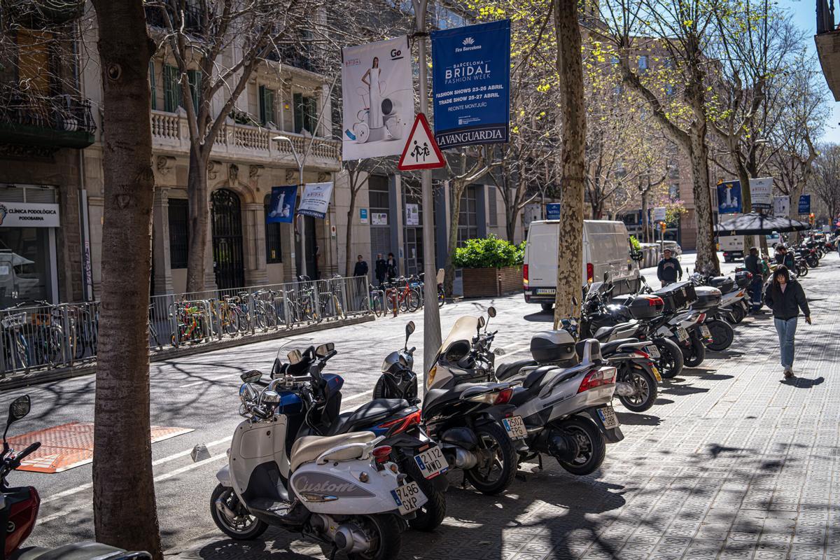 Motos estacionadas en la acera, bajo el cartel de zona escolar, frente a la Escola Diputació.