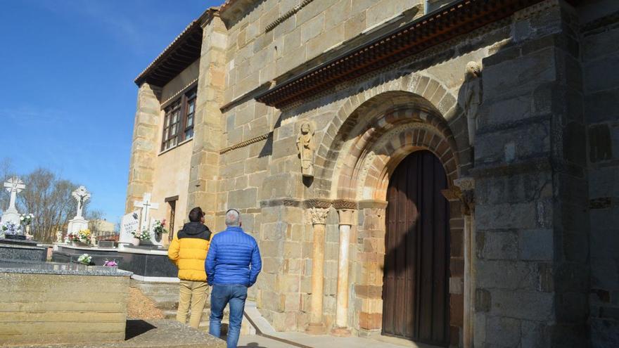 Dos visitantes a Santa Marta de Tera contemplan el Santiago Peregrino en la cabecera del templo, rodeada del cementerio ya clausurado. | E. P.