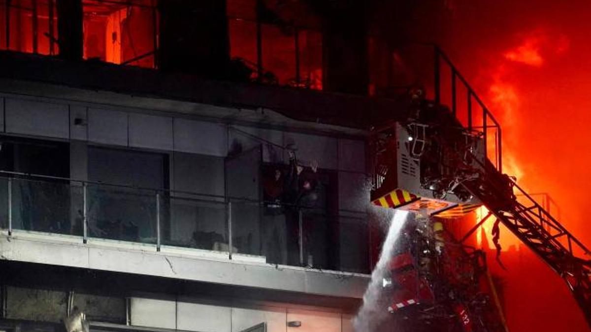 Un bombero trata de apagar el edificio en llamas con dos personas en un balcón, en el incendio de Valencia