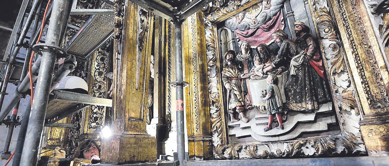 Una escena tallada en el retablo de Santa María; a la izquierda, asomando entre el andamiaje, Belén García.