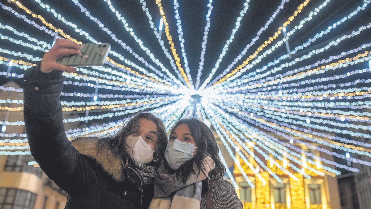 Dos jóvenes con mascarilla se hacen una foto junto a las luces de Navidad de la Plaza Mayor de Zamora.