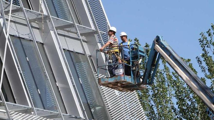 Dos operarios trabajan en la estructura metálica que envuelve el edificio.