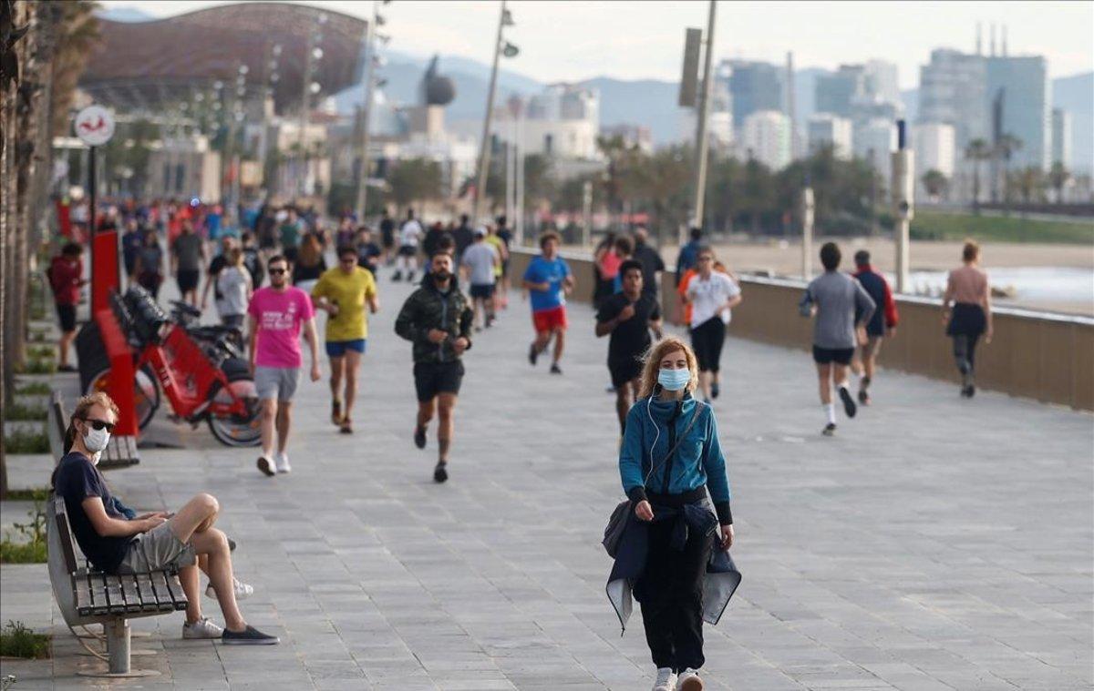 Una mujer con mascarilla pasea, entre deportistas, por el paseo Marítimo de la Barceloneta.