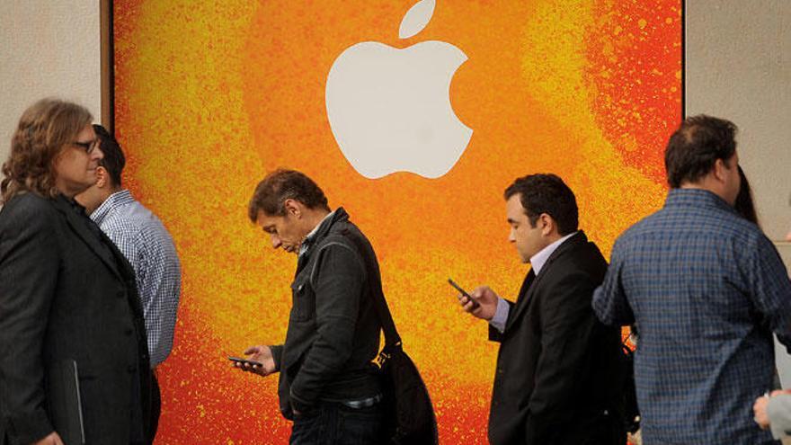 Dos personas consultan su móvil ante una tienda de Apple.