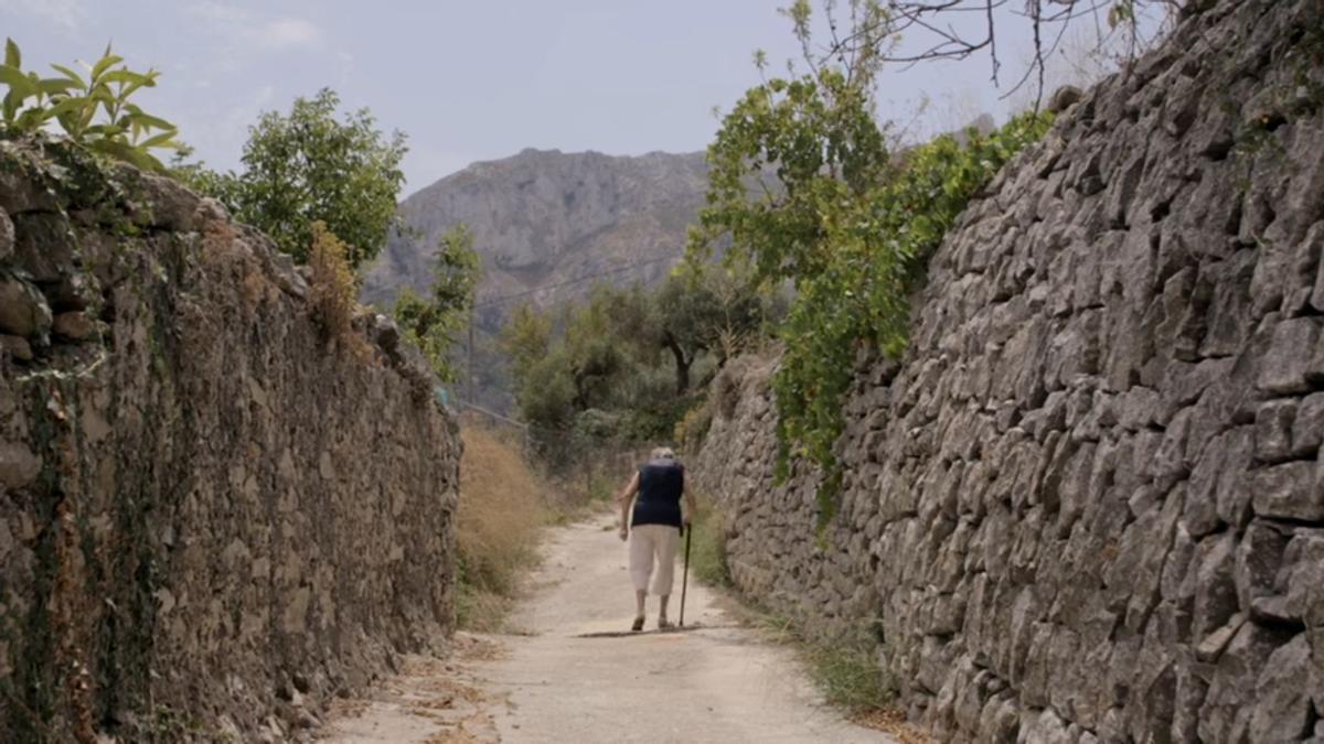 Una anciana de la Vall de Gallinera camina entre los muros de piedra seca. Es una de las poéticas imágenes del documental