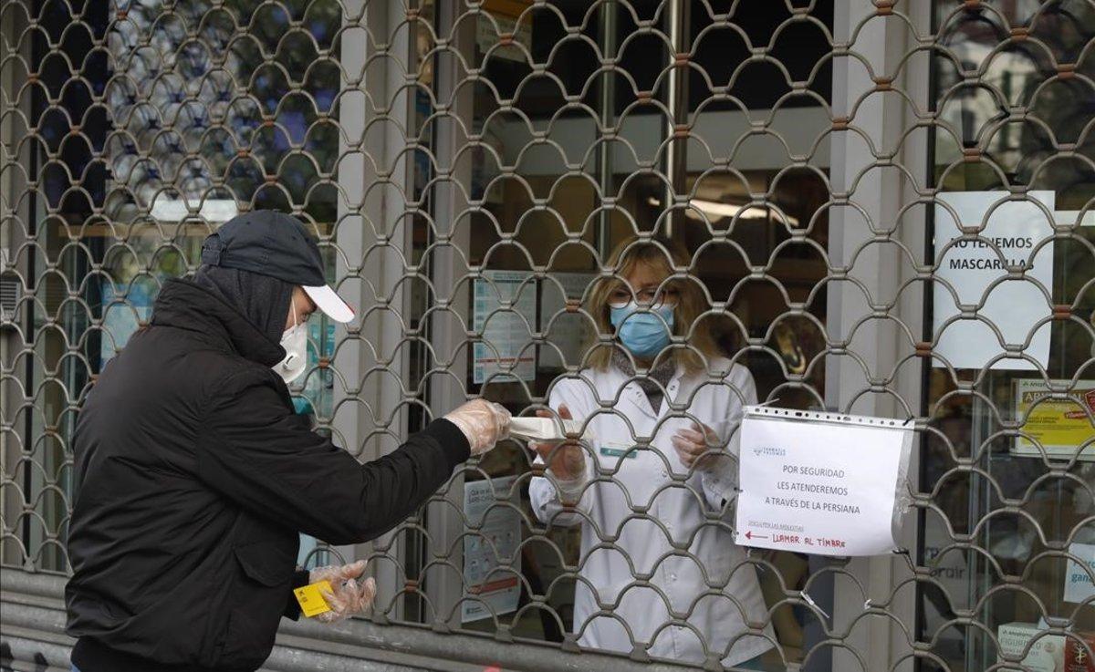 Una farmacia despacha a través de la persiana cerrada en el barrio barcelonés de Sant Andreu.