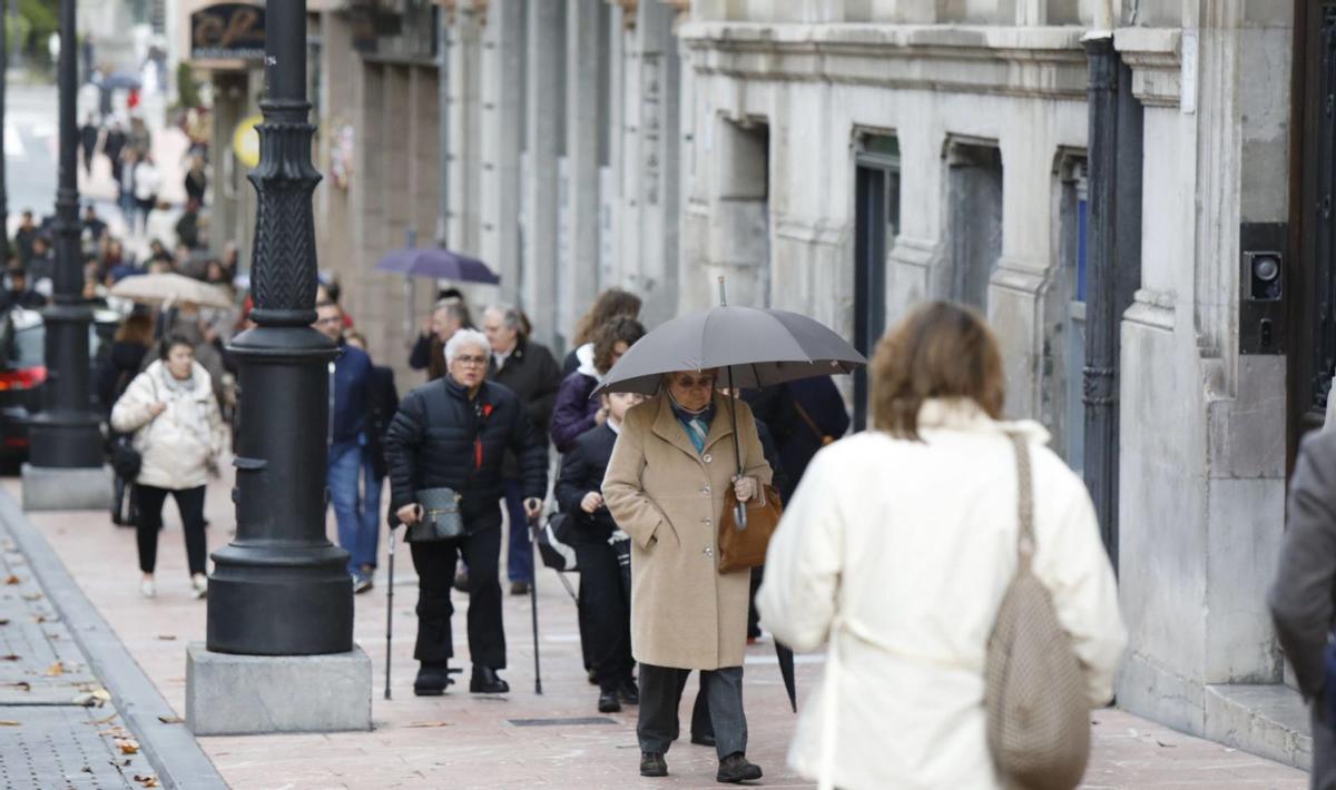 Paseantes con abrigos y paraguas, por el centro de Oviedo. | Fernando Rodríguez