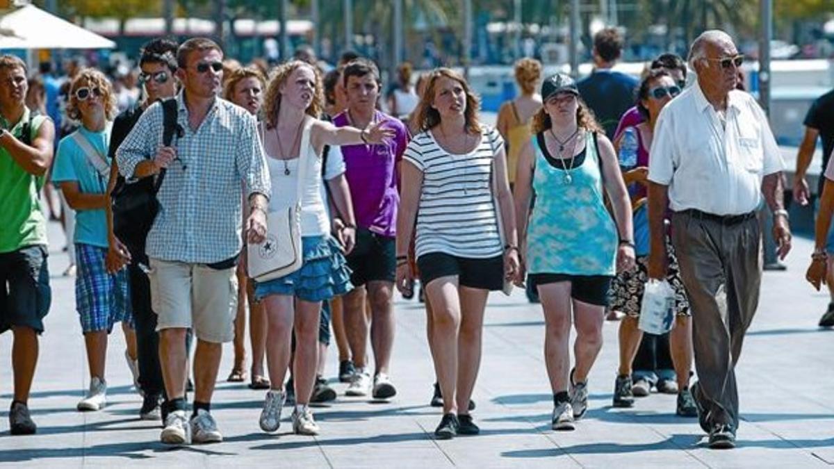 Un grupo de turistas, provisto de gafas de sol y calzado deportivo, pasea bajo el sol por el Port Vell, ayer por la mañana.