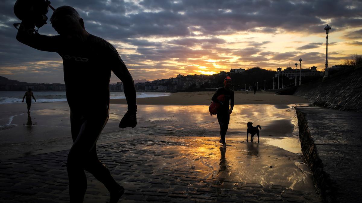 Dos hombres salen del agua al amanecer en la playa de Ondarreta de San Sebastián.