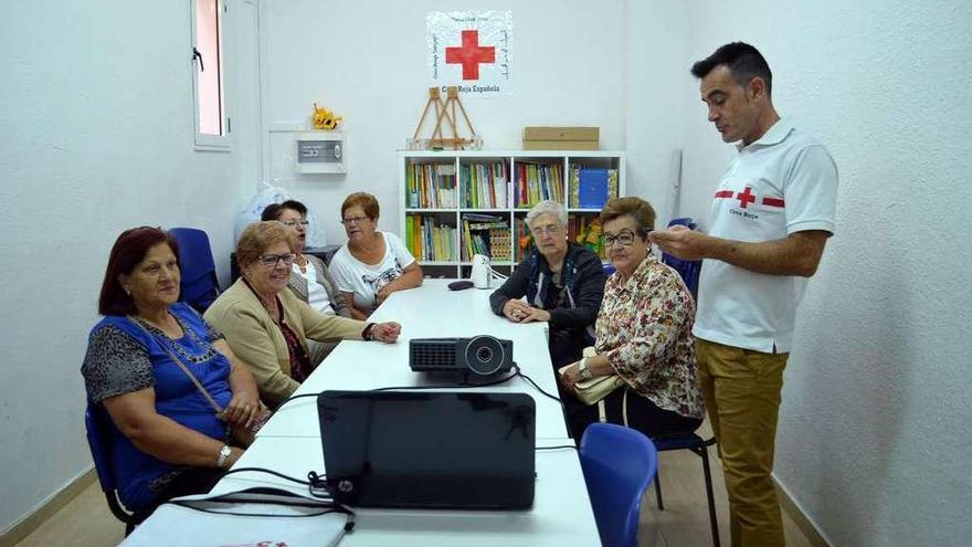 Un técnico de Cruz Roja, de pie, ofrece un curso de primeros auxilios a un grupo de mayores.