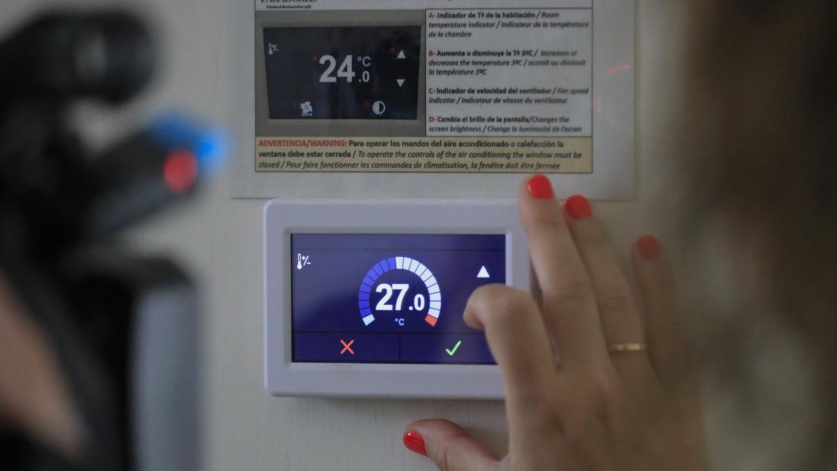 Eine Frau stellt einen Thermostat auf 27 Grad ein, um die Energiesparmaßnahmen zu erfüllen.