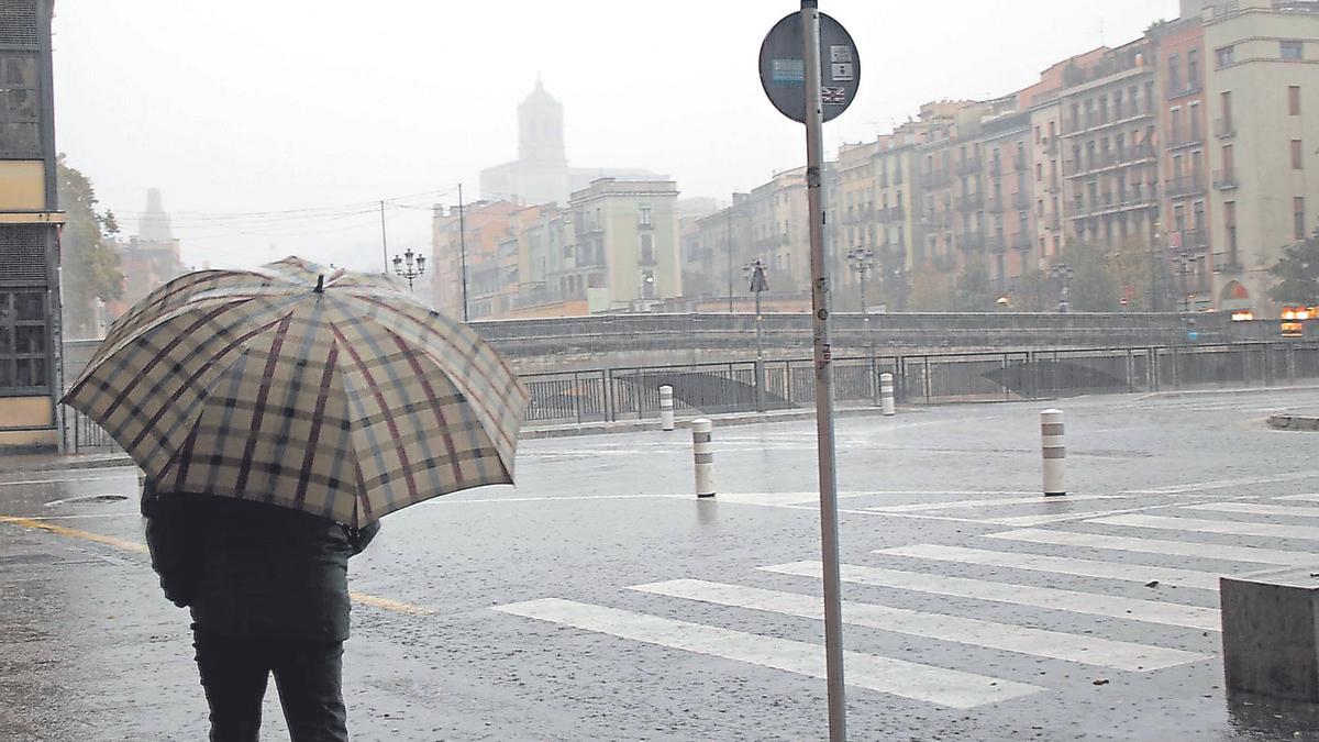 Un home amb un paraigua passeja sota la pluja, a Girona, en una imatge d’arxiu.