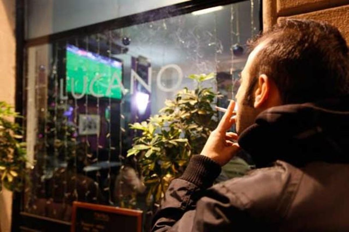 Un fumador, a l’exterior d’un restaurant a Barcelona, segueix el partit de futbol des del carrer en el primer dia en què entra en vigor la nova llei antitabac