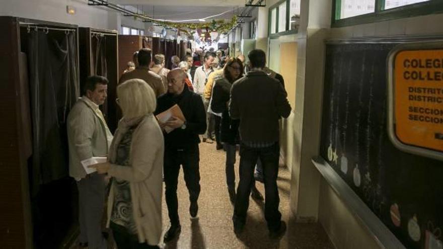 Imagen de un colegio electoral con las cabinas de votación en las que ejercen su derecho al voto varias personas y varios electores depositan su voto.