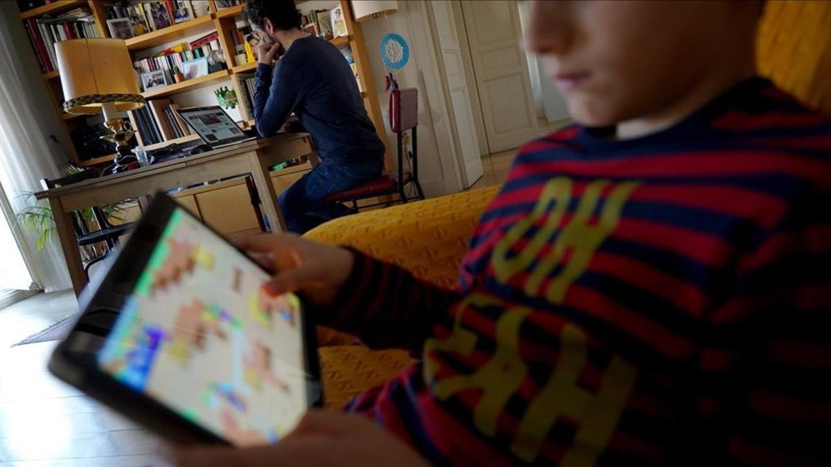 Un padre teletrabja mientras su hijo juga con el iPad, hoy en Madrid.