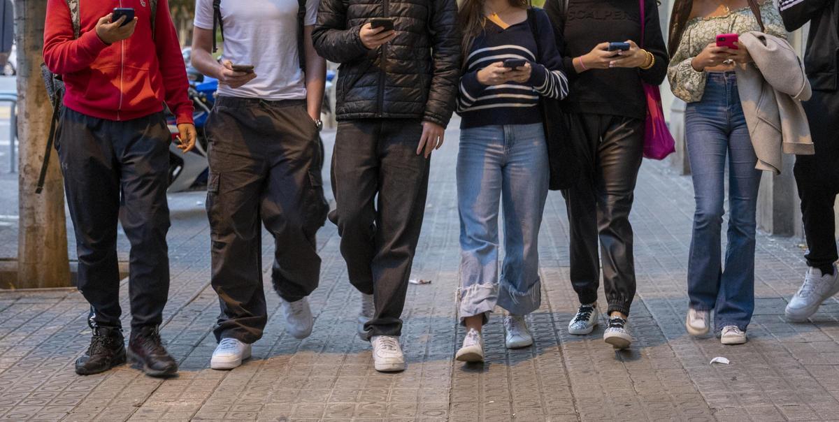 Barcelona. 13.11.2023. Sociedad. Jóvenes atentos a las pantallas de sus móviles a la salida del instituto. Fotografía de Jordi Cotrina. FOTO DE RECURSO. MENORES. USO. TELEFONOS MOVILES. PANTALLAS. INTERNET. REDES SOCIALES. RIESGOS