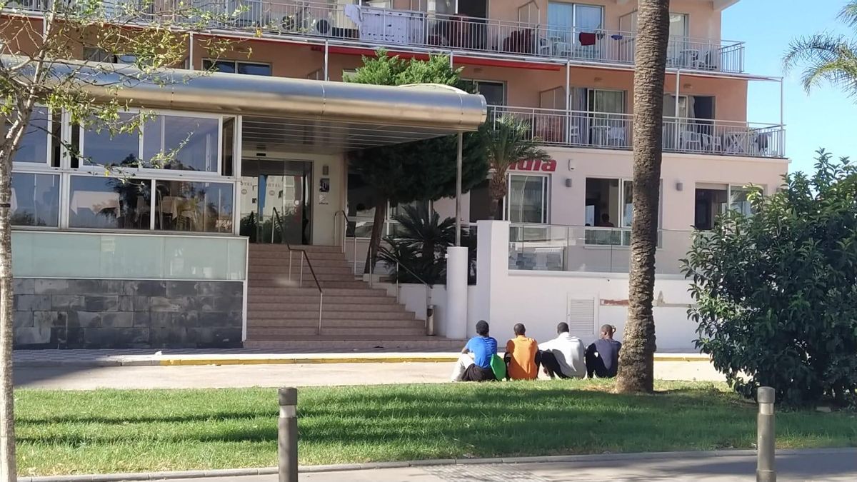 Varios jóvenes migrantes sentados frente a uno de los hoteles de Gandia donde se alojan