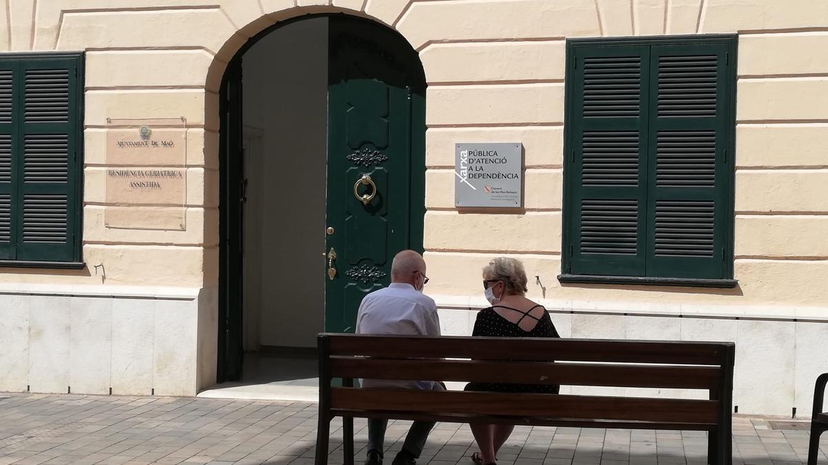 Archivo - Dos personas mayores conversan sentadas en un banco y con mascarilla, ante una Residencia