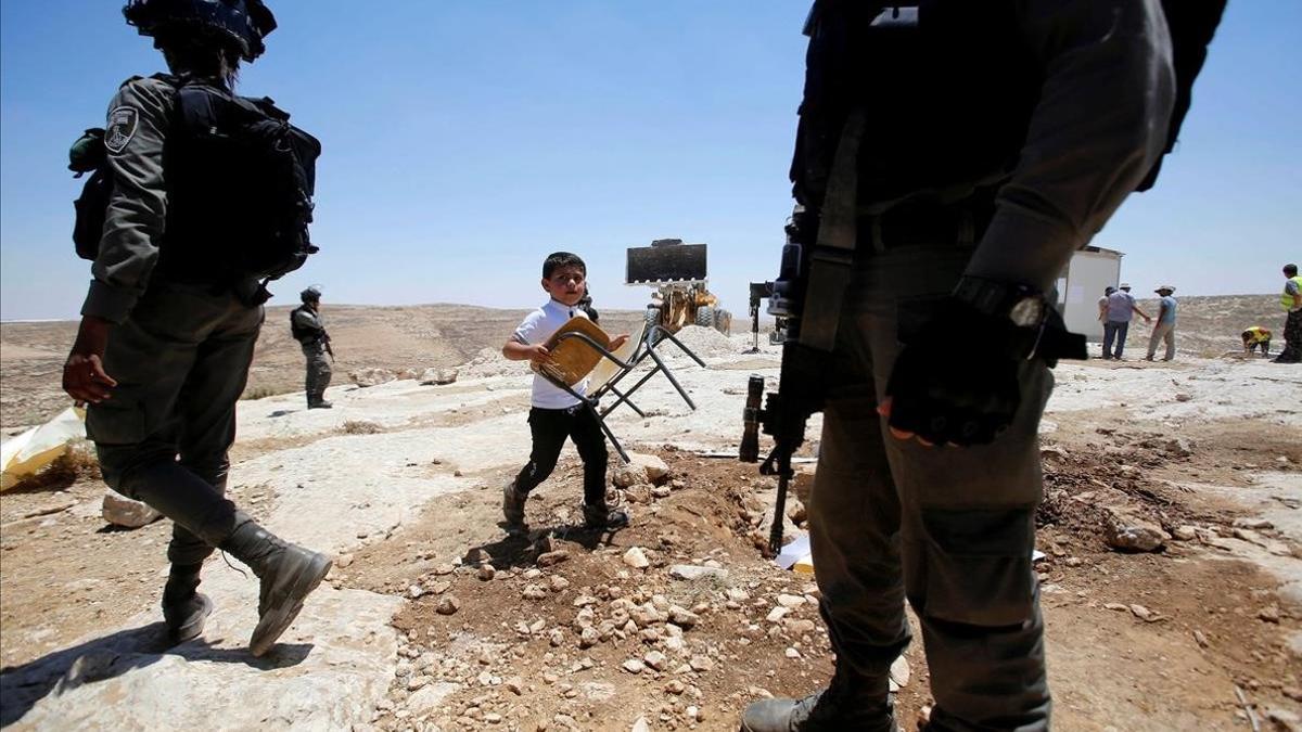 Un niño palestino pasa junto a soldados israelís camino de la escuela, cerca de Hebron.