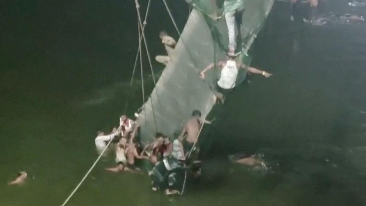 La gente se aferra al puente colgante colapsado en Morbi, India.