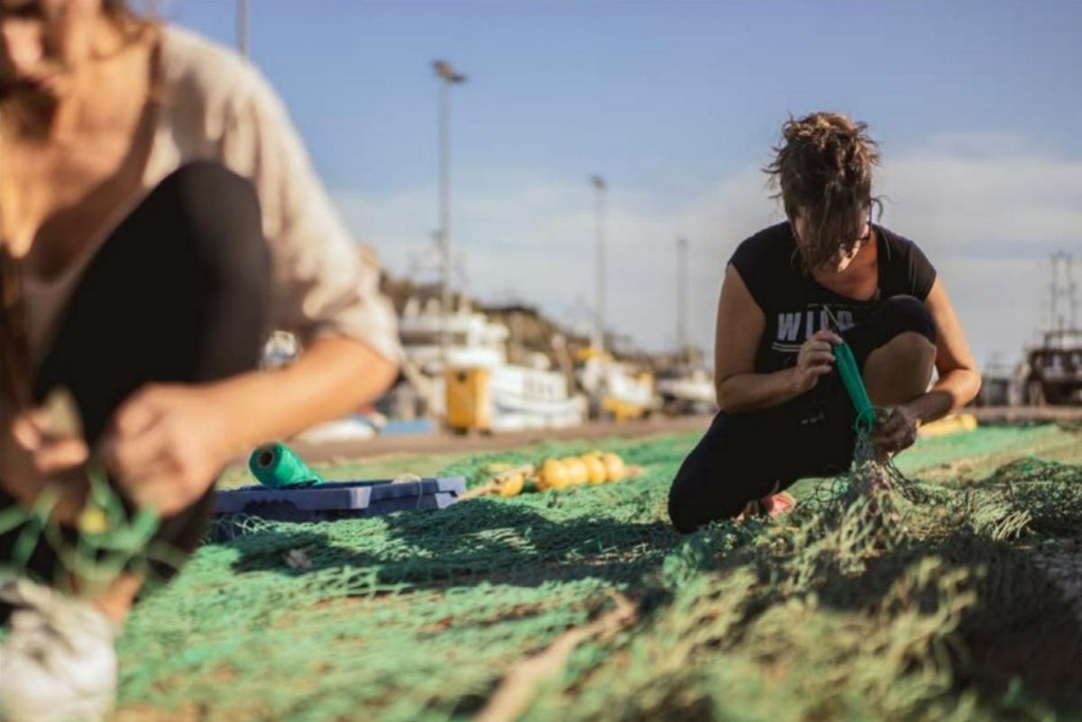 Unas mujeres reparan unas redes de pesca en el puerto.