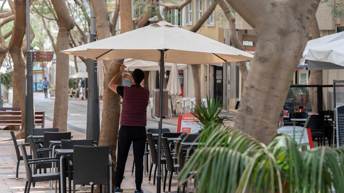 Un camarero abre la sombrilla de un bar.