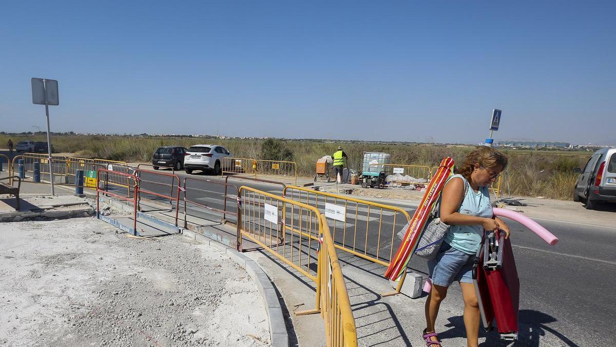 Una mujer, cargada con la sombrilla y la hamaca, sortea las obras en aceras en Urbanova, que arrancaron este verano