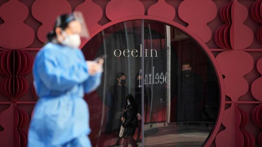 Una mujer con ropa protectora pasa frene a una tienda en Shanghái, en China, país que abandonó este año la estrategia “cero COVID”.