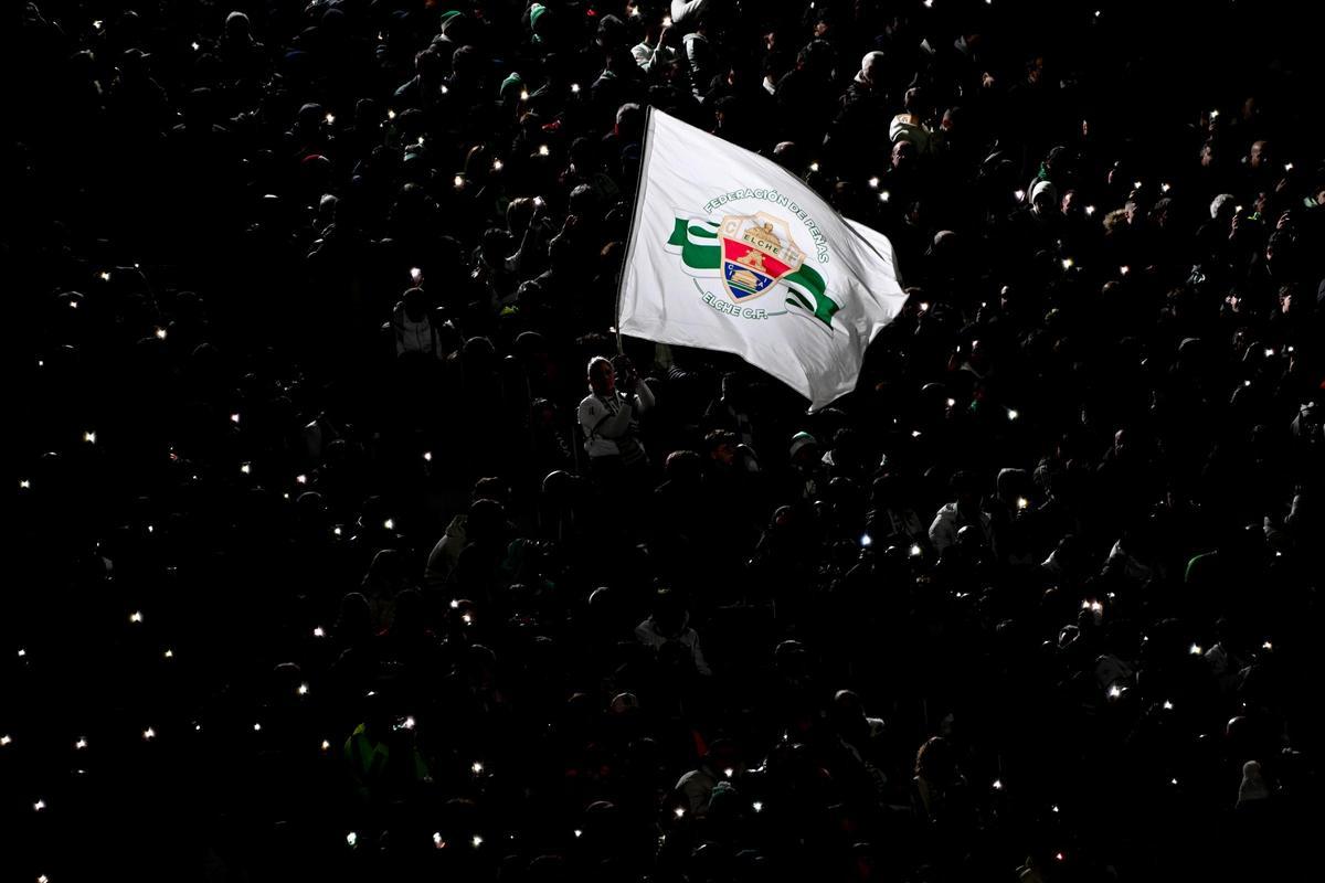 Una bandera con el escudo del Elche es hondeada en las gradas del Martínez Valero, con las luces del estadio apagadas.