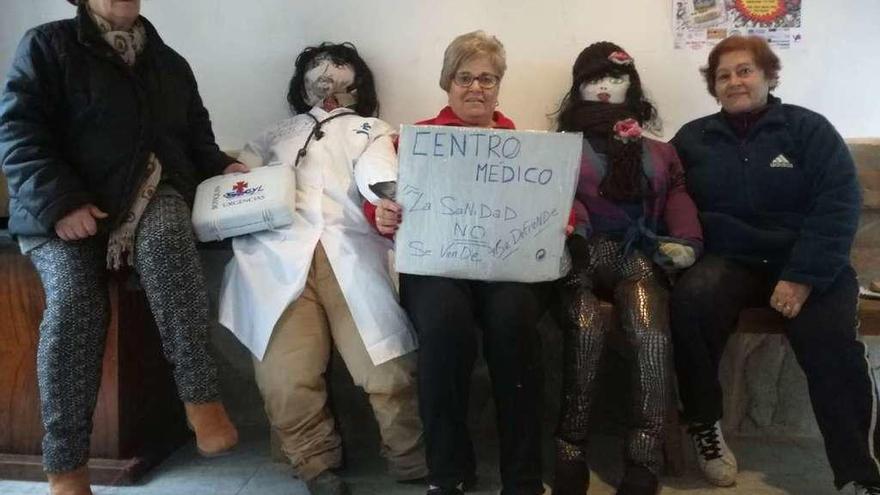 Tres mujeres posan con los muñecos del Mayo en La Milla y reivindican mejoras en la sanidad rural.