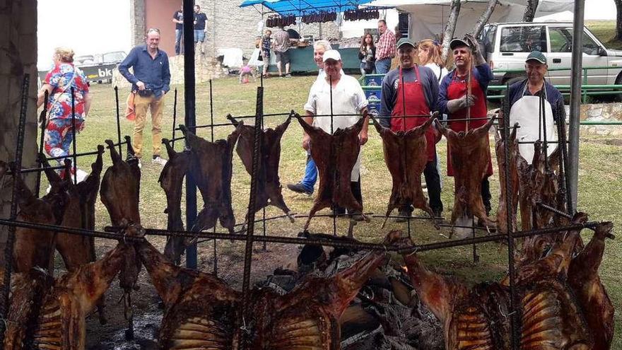 Los asadores Tomás Argüelles, Chema Fernández, Javier Rodríguez y Roberto González, junto a los corderos. A la izquierda, ambiente de fiesta.