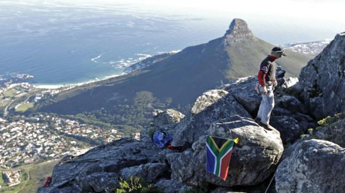 Un home domina Ciutat del Cap des de Table Mountain, on ha col·locat la bandera sud-africana.