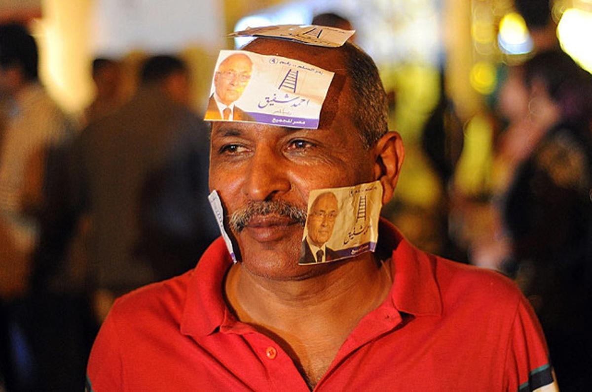 Un ciutadà es posa a la cara adhesius del canditat a les eleccions presidencials d’Egipte Ahmed Xafiq, després d’un incendi provocat que ha afectat la seu del partit al Caire.