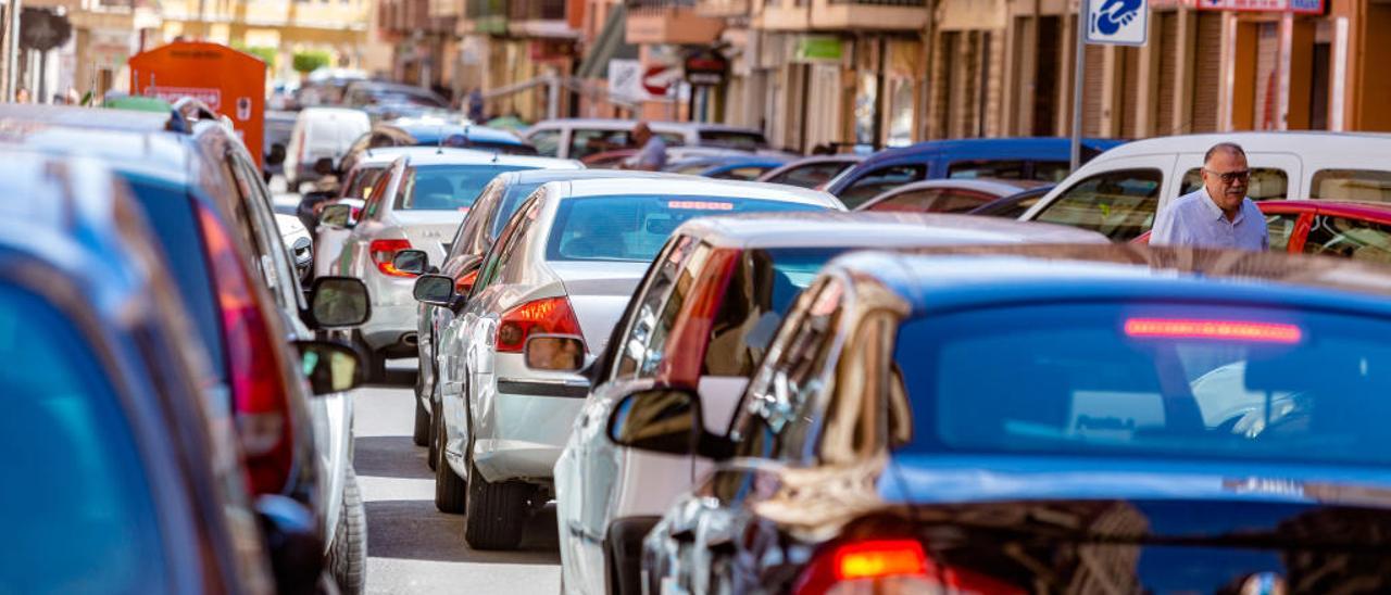 Denso tráfico en las calles del municipio, con coches en doble fila y vecinos sorprendidos.