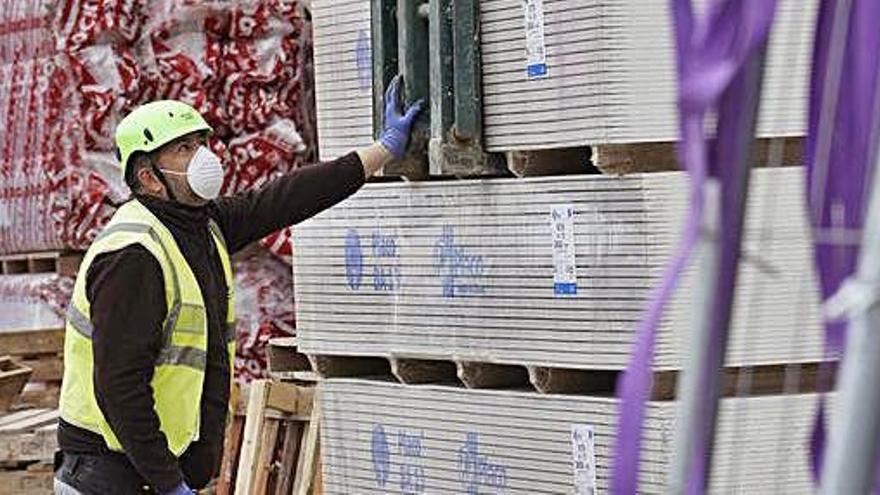 Un treballador carrega material a la grua, a Girona. Obrers finalitzant una paret.