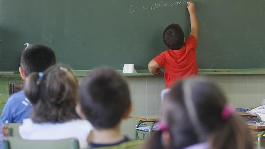 Un alumno escribe en la pizarra mientras sus compañeros prestan atención.