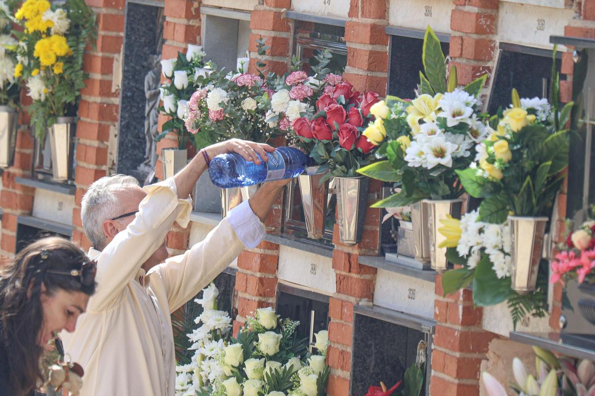 Un hombre echa agua en el búcaro donde ha colocado unas bonitas flores junto a una lápida.
