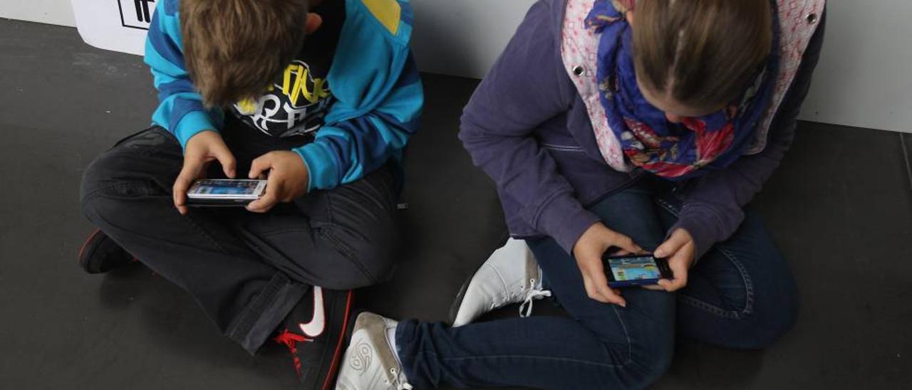 Dos niños miran sus móviles.