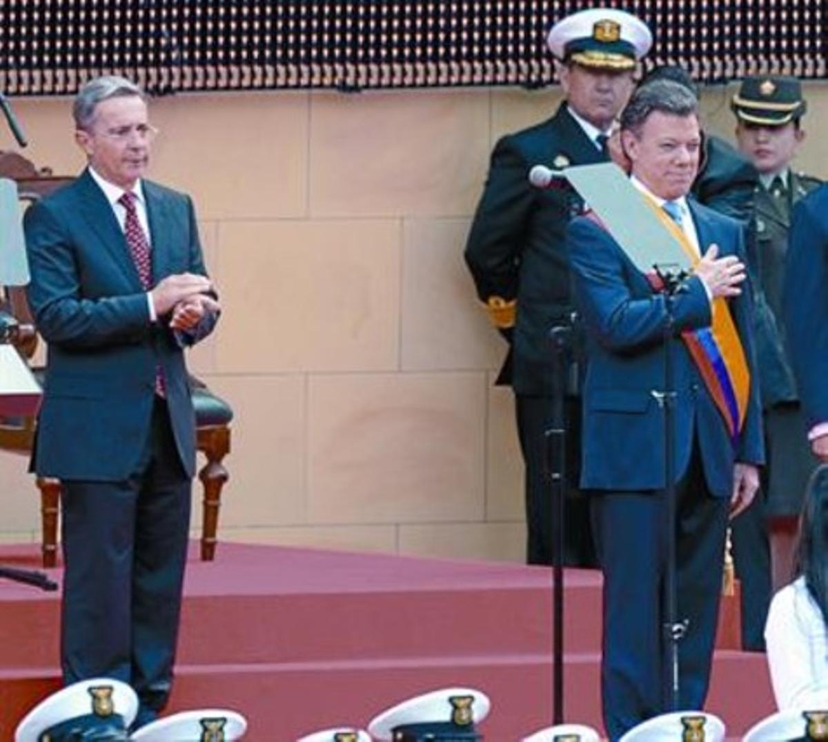 Uribe, a la izquierda, aplaude a Santos después de que anoche tomara posesión de la presidencia.