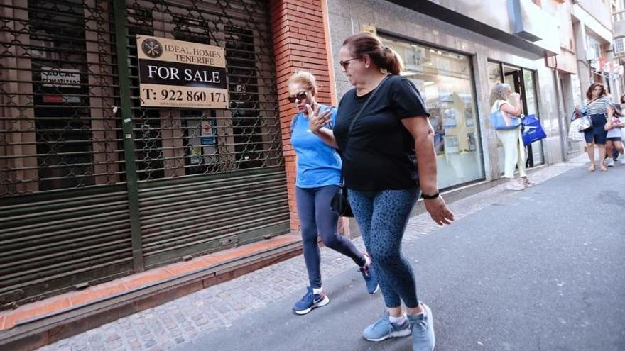 Dos mujeres pasan en Santa Cruz de Tenerife ante un cartel de ‘Se vende’, en inglés, de una inmobiliaria. | |