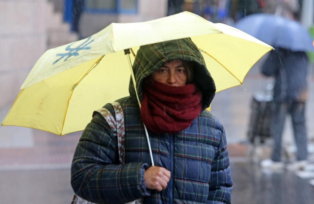 Viandantes tratan de protegerse de la lluvia, en el centro de Vigo