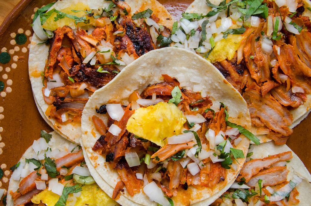 Los tacos al pastor se sirven con piña, cebolla y cilantro.
