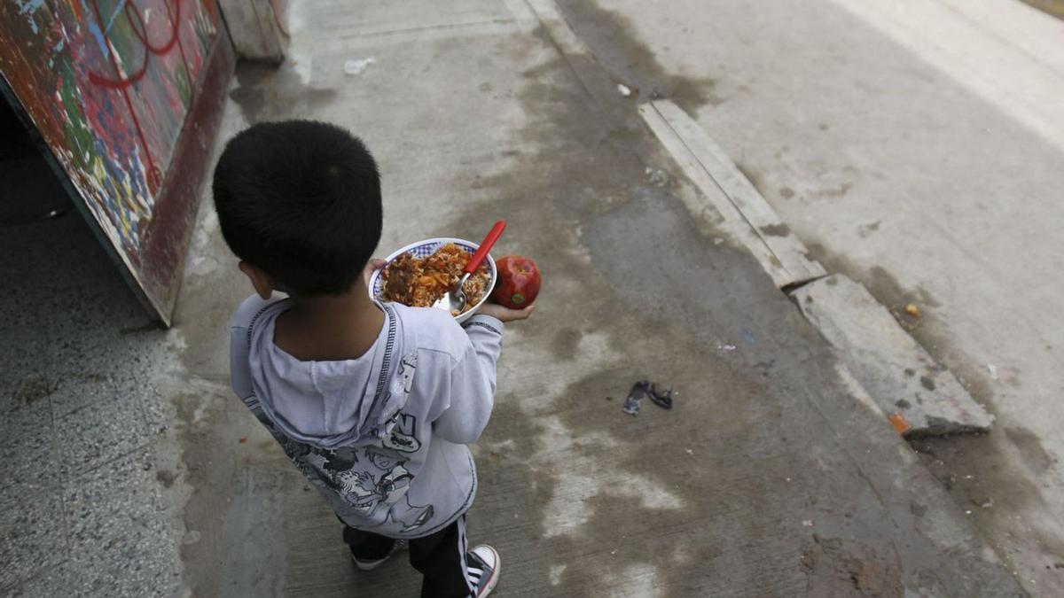 Un niño sostiene un plato de comida y una manzana. |   // DAVID FERNÁNDEZ